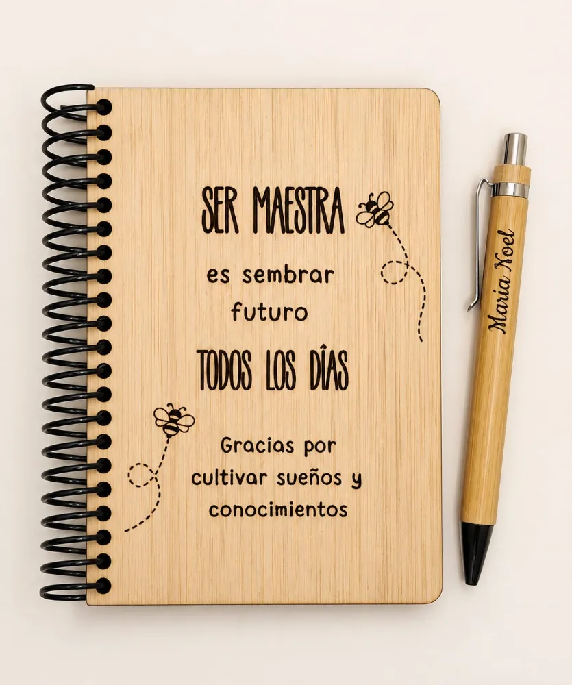 Libreta de madera clara grabada con una frase entera para una maestra, junto a una lapicera de bambú.