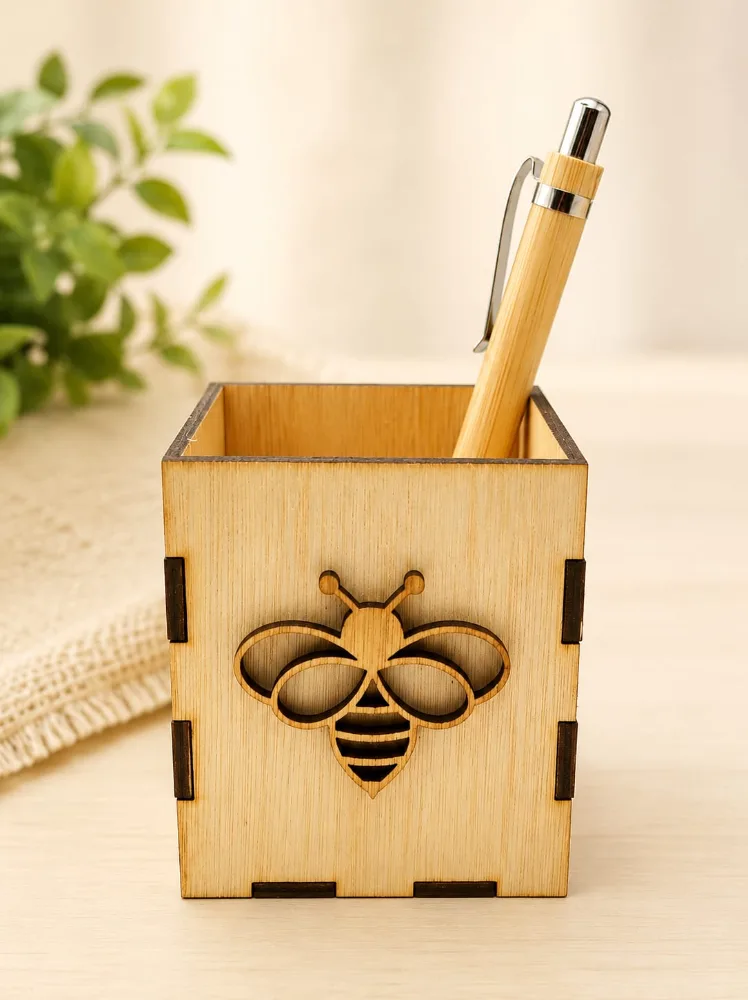 Portalápices cúbico de madera con una abeja calada en el frente y una lapicera de bambú adentro.
