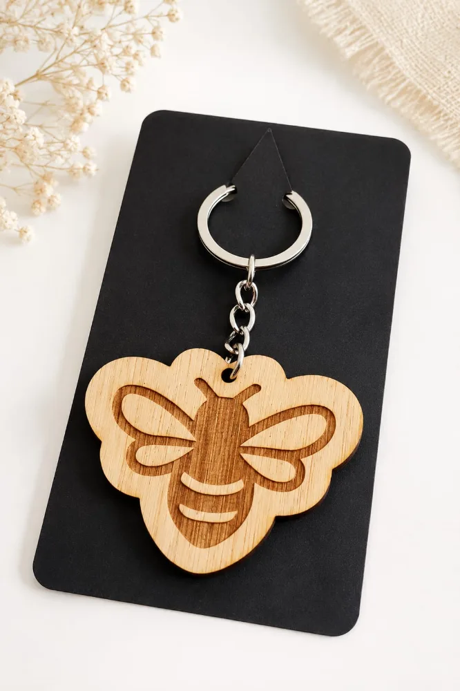 Llavero de madera con forma de abeja grabada, presentado sobre una tarjeta negra.