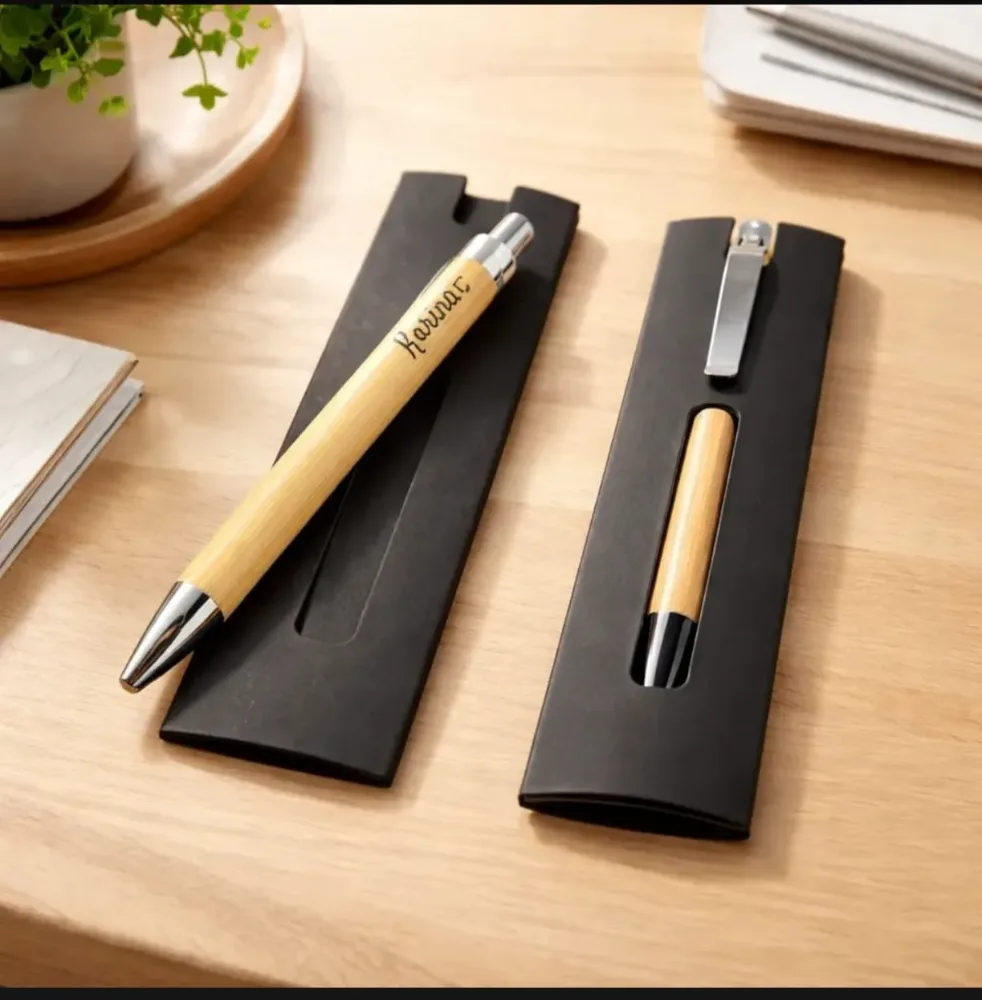 Dos estuches de papel negro sobre un escritorio de madera: uno con una lapicera de bambú grabada encima y otro con la lapicera adentro.